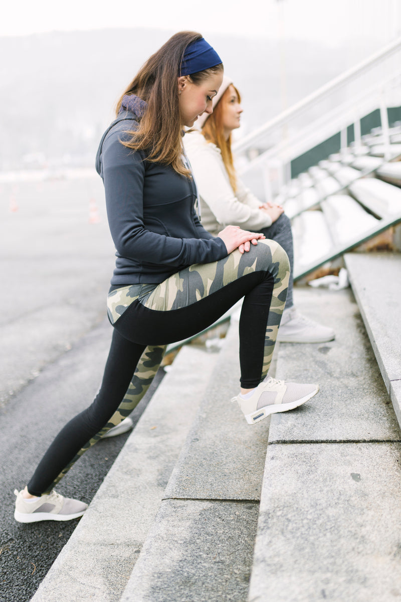 Two women warming up and stretching on bleacher steps before a workout.