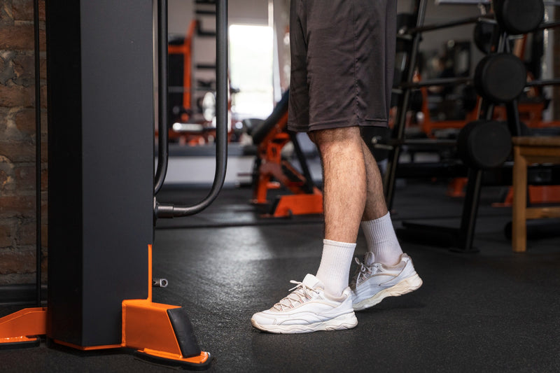 A person in a gym wearing white athletic socks and white sneakers, standing next to a exercise machine.