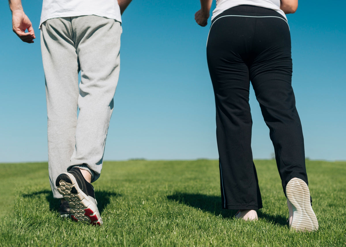 Two people walking away on a grassy field under a clear blue sky.