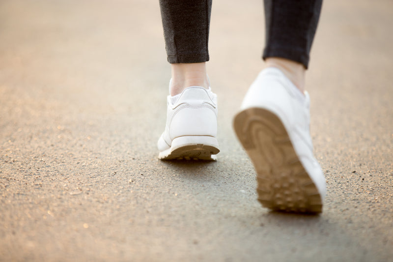 Close-up from behind of a person walking in white sneakers.