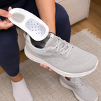 A person holding a light gray shoe insert in their hand, demonstrating a shoe insole or cushioning insert.