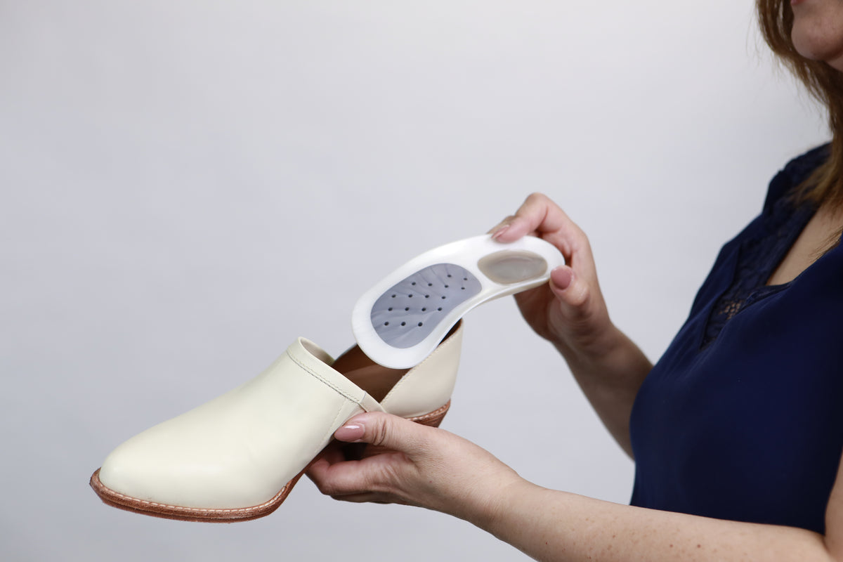 Close-up demonstration of a white WalkFit Platinum orthotic shoe insert fitting easily into a casual dress shoe.