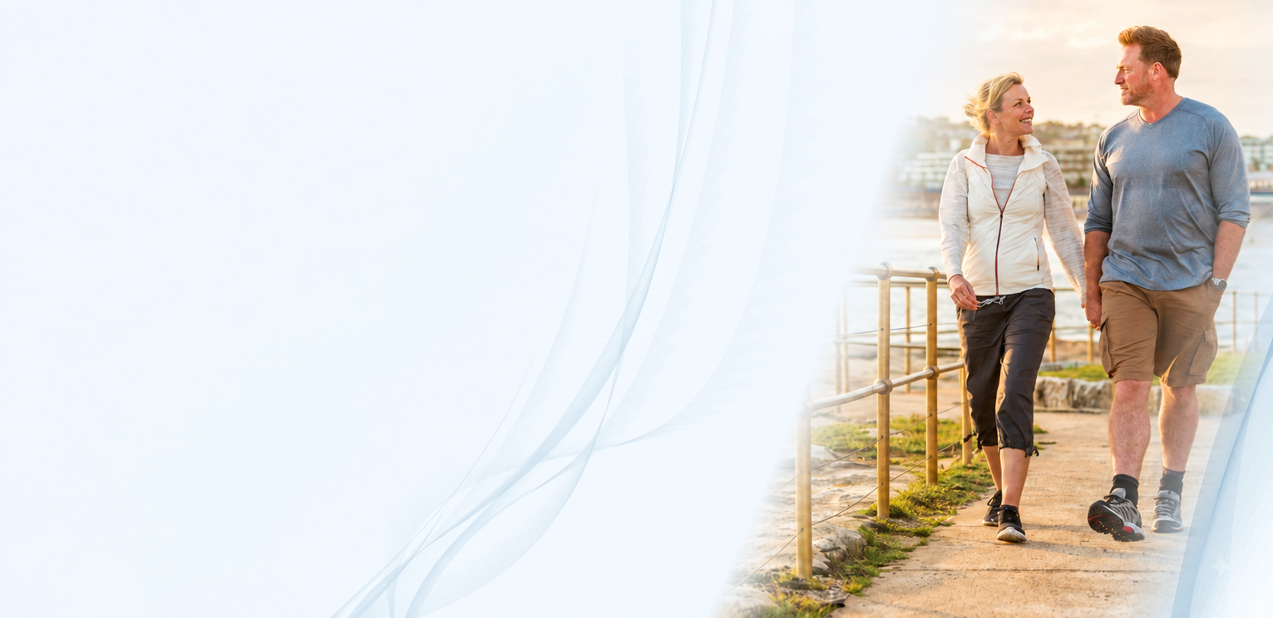 A man and a woman walking hand in hand along a sunlit outdoor path.